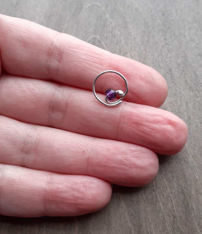 Earring with amethyst bead on a hand.