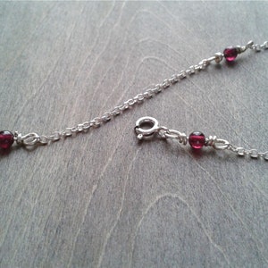 Garnet bracelet against a wooden background. Detail of the round clasp.