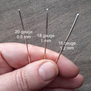 A hand holds 3 pieces of silver representative of the 3 gauges in which this earring is offered: 20 gauge (0.8 mm); 18 gauge (1 mm); 16 gauge (1.2 mm).