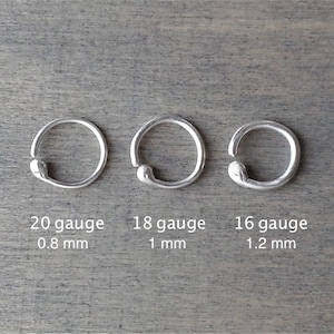 3 sterling silver hoops against a wooden background. They are is 3 different gauges (thicknesses): the 20 gauge hoop is 0.8 mm thick; the 18 gauge hoop is 1 mm thick; the 16 gauge hoop is 1.2 mm thick.