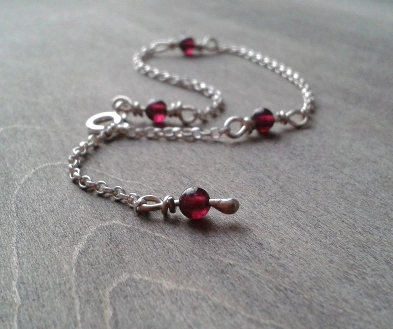 Garnet bracelet against a wooden background. Garnet beads are added at even intervals through the chain that forms this bracelet. One of the links of the chain is used to close the bracelet.