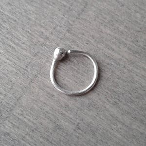 Sterling silver hoop against a wooden background. One end of the hoop has been worked with a torch to form a rounded ball.