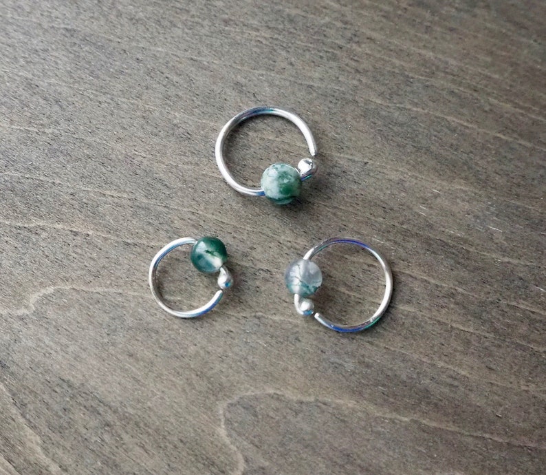 Three sterling silver hoops with bead of moss agate on wooden background. This hoop is offered with moss agate  in a variety of colors and textures