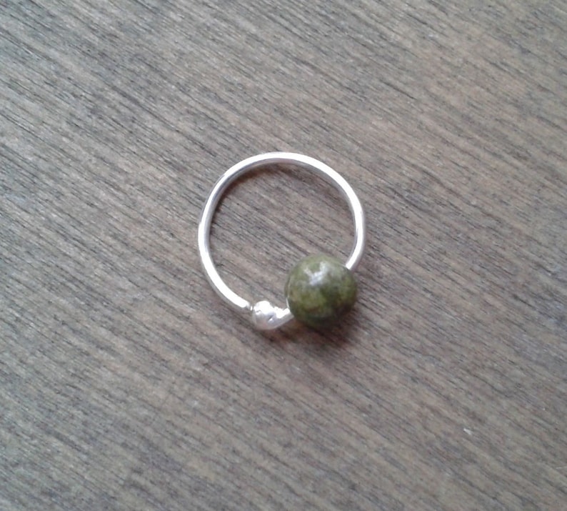 Sterling silver hoop with a dragon's blood bead against a wooden background. The hoop is made from a single piece of wire. One of its ends forms a small ball of silver to hold in the bead that is threaded through.