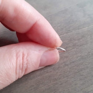 Brilliant hoop earring held by a hand to show the hammering on the outside of the hoop.