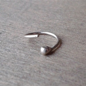 Sterling silver hoop against a wooden background. The hoop is open sideways. There is no hinge or other device to open and close the hoop. The softness of the metal allows it to be opened and closed.