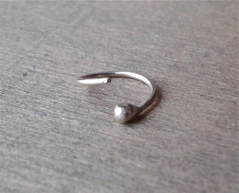 Sterling silver hoop against a wooden background. The hoop is open sideways. There is no hinge or other device to open and close the hoop. The softness of the metal allows it to be opened and closed.