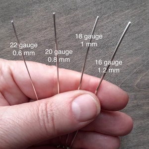 A hand holding pieces of silver in different gauges: 22 gauge is 0.6 mm thick; 20 gauge is 0.8 mm thick; 18 gauge is 1 mm thick; 16 gauge is 1.2 mm thick.