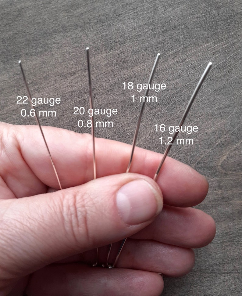 A hand holding pieces of silver in different gauges: 22 gauge is 0.6 mm thick; 20 gauge is 0.8 mm thick; 18 gauge is 1 mm thick; 16 gauge is 1.2 mm thick.