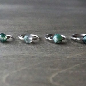 Four sterling silver hoops with bead of moss agate on wooden background.