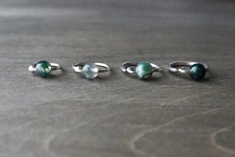 Four sterling silver hoops with bead of moss agate on wooden background.