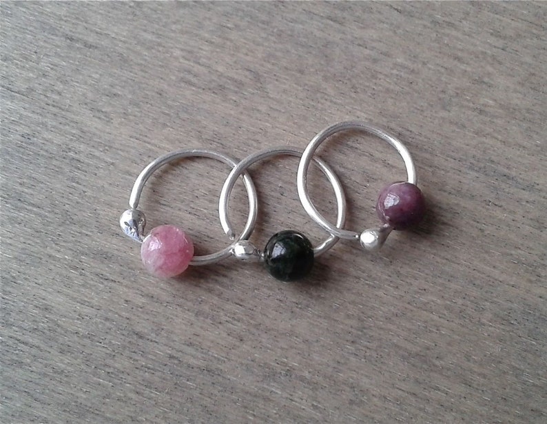 Tourmaline hoops against a wooden background. Each hoop is formed form a single piece of sterling silver. One end of the hoop is formed into a small ball of silver to hold the bead and keep it from falling off. The bead is threaded through.