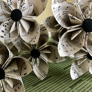 May include: A bouquet of origami flowers made from sheet music. The flowers are white with black musical notes and have black centres.