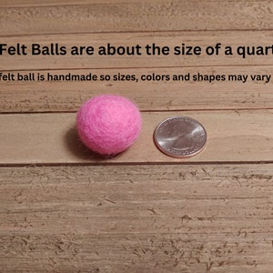 May include: A pink felt ball next to a US quarter, showing the size of the felt ball. The text "Felt Balls are about the size of a quarter. Each felt ball is handmade so sizes, colors and shapes may vary slightly." is visible above the felt ball and quarter.