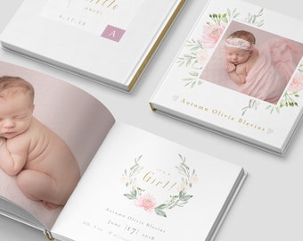 May include: A white baby photo album with a floral design and the text "It's a Girl!" on the cover. The album is decorated with pink and green watercolor flowers. The text "Autumn Olivia Blevins" is printed on the cover. The album is closed and lying flat on a white surface.