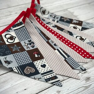 Può includere: Uno stendardo di tessuto con un design a patchwork che presenta cuori, stelle e motivi a scacchi in tonalità di marrone, blu e bianco. Lo stendardo è rifinito con un nastro rosso e ha un bordo smerlato.