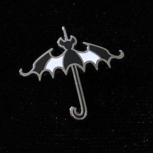 May include: A silver-colored pin shaped like a bat with black and white wings, holding an umbrella.