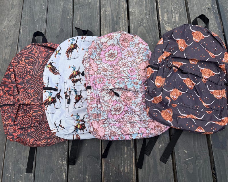 K&ouml;nnte beinhalten: Vier Rucks&auml;cke mit verschiedenen Mustern: einer mit dunkelorangem Blumenmuster, einer mit wei&szlig;em Cowboy- und Pferdemotiv, einer mit rosa-wei&szlig;em Blumendesign und einer mit schwarzem Hintergrund und braunen Highland-Rind-Illustrationen.