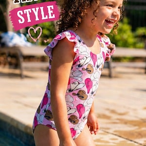 K&ouml;nnte beinhalten: Ein junges M&auml;dchen tr&auml;gt einen rosa Badeanzug mit Cowboyhut-Muster und planscht in einem Pool. Der Badeanzug hat R&uuml;schen&auml;rmel. Der Text "CUSTOMER FAVORITE STYLE" ist im Bild zu sehen.