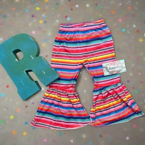 Stay Wild Girls Bell Bottom Set. Features a black Fringed Shirt with a bold "Stay Wild" design in pink and cheetah print, perfectly paired with vibrant serape-striped bell bottoms. Ships FREE with $35+ purchase.