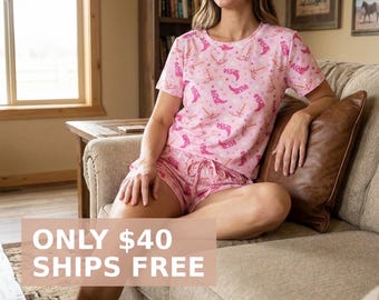 May include: Pink pajama set with a pattern of cowboy boots and anchors. The short-sleeved top and shorts are made of a soft material. The shorts have a drawstring waist. The pajama set is designed for comfort and relaxation.