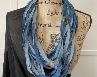 May include: A denim necklace made from strips of blue denim fabric. The necklace is layered and has a frayed edge.