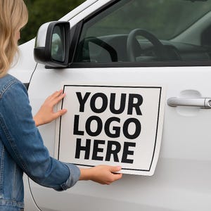 May include: A white rectangular sign with the text "YOUR LOGO HERE" in bold black letters is being placed on a white car door. The car has a black side mirror and a silver door handle. The background is blurred.