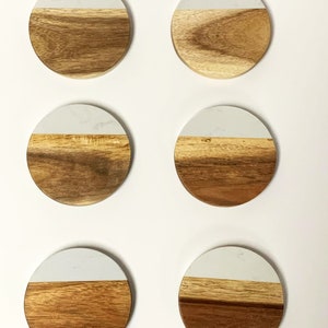May include: Six round coasters made of wood and white marble. Each coaster has a white marble top and a brown wood bottom.