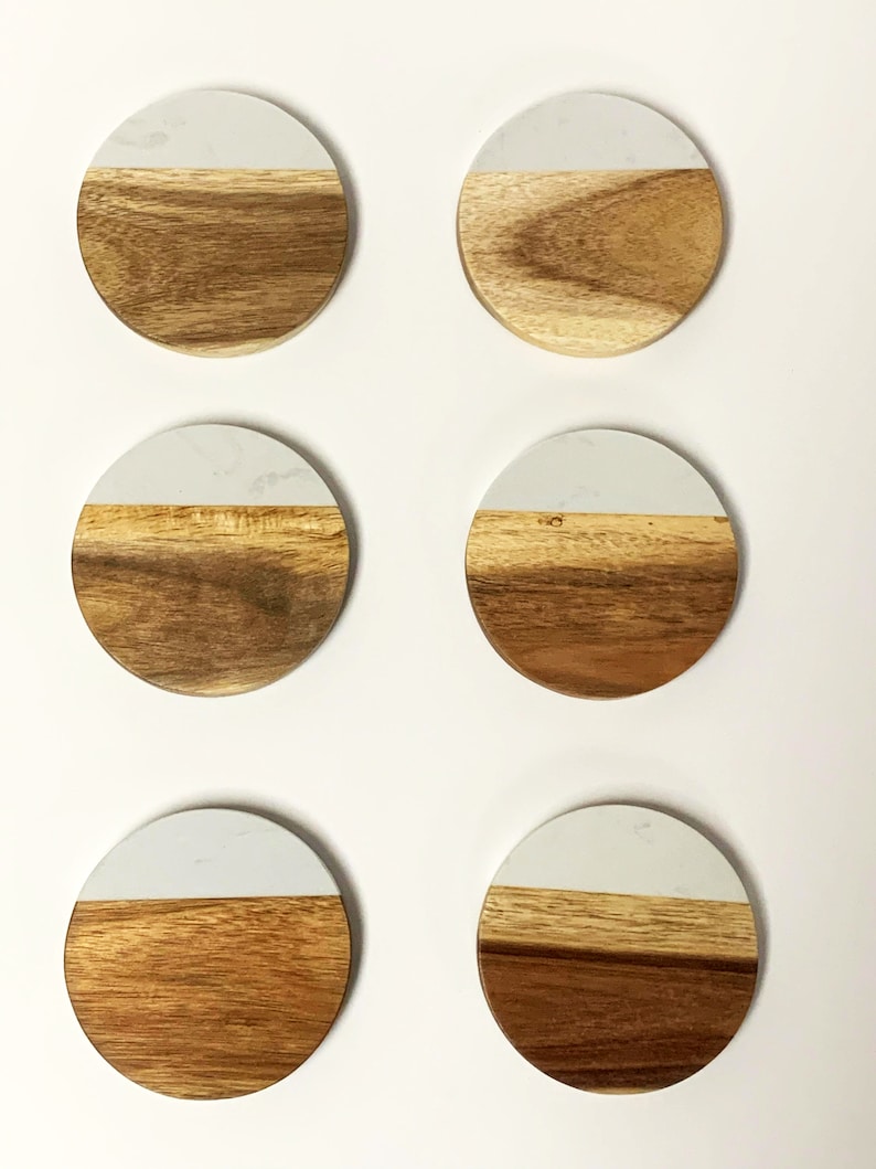 May include: Six round coasters made of wood and white marble. Each coaster has a white marble top and a brown wood bottom.