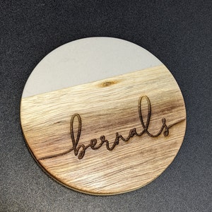 May include: A round wooden coaster with a white top and the word "bernals" engraved in the wood.