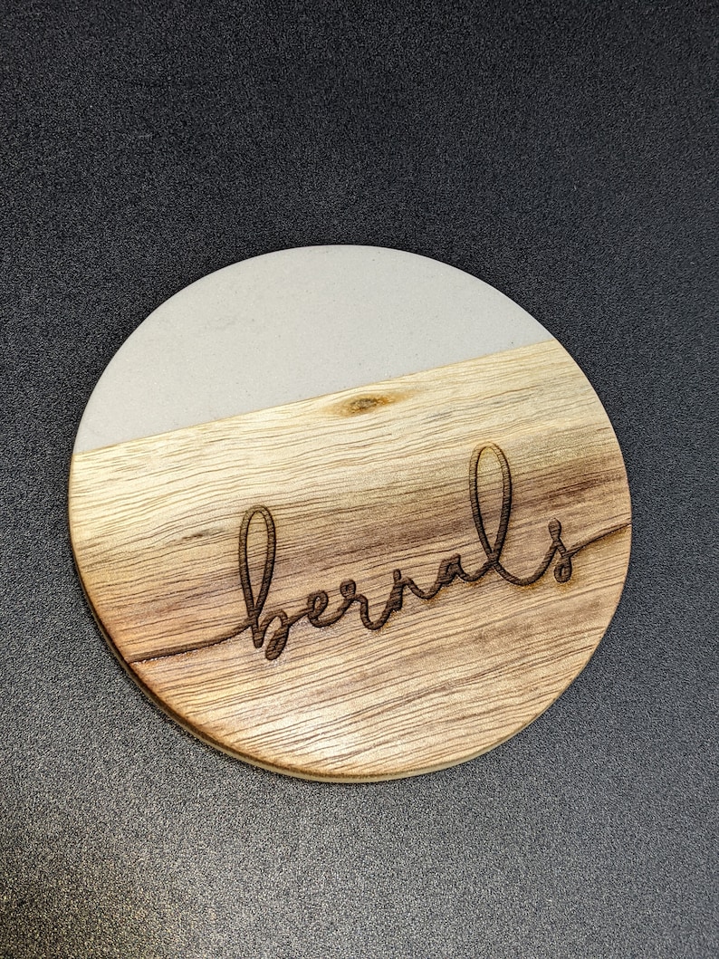 May include: A round wooden coaster with a white top and the word "bernals" engraved in the wood.