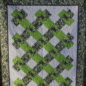 May include: A green and grey quilt with a geometric pattern. The quilt is quilted with a swirl design and has a white background.