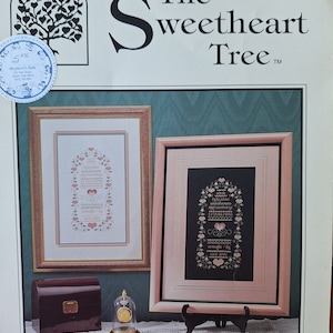 May include: A cross stitch pattern titled "The Sweetheart Tree" with two framed cross stitch designs. The designs are in pink, green, and black thread. The text "Ebony and Ivory" is at the bottom of the image.
