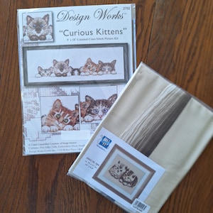 May include: A cross stitch kit featuring a design of three kittens with the title "Curious Kittens". The kit includes 14 count Aida cloth, embroidery floss, a needle, and instructions. The kit is from Design Works Crafts.