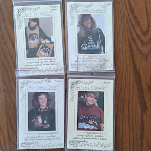 May include: Four vintage sewing pattern packets featuring winter-themed appliqued sweatshirts. The packets include images of the finished garments and the phrases "Let It Snow!", "Ice Skate'n Escapades", "Christmas Past", and "And To All A Goodnight."