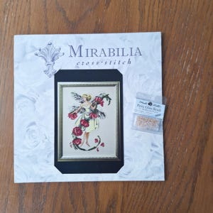 May include: A Mirabilia cross-stitch pattern booklet featuring a fairy illustration with wings and red flowers, accompanied by a small clear plastic packet of Mill Hill petite glass beads for needlework projects, labelled with the number 42027.