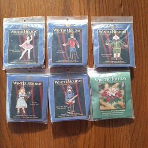 May include: Six different Winter Holiday bead kits featuring various Christmas characters and a poinsettia. Each kit includes a counted glass bead kit with a treasure. The finished size of each kit is 6.35 cm by 11.43 cm.