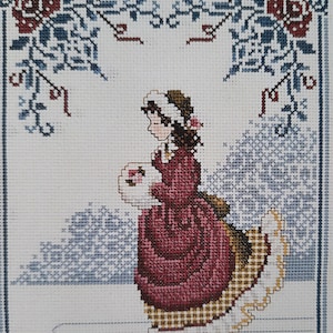 May include: Cross-stitch pattern of a girl in a red dress and white hat ice skating on a snowy background with a floral border.