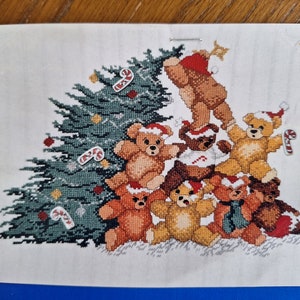 May include: A cross-stitch pattern featuring a Christmas tree with candy canes and a group of teddy bears wearing Santa hats.