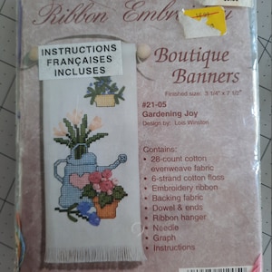 Könnte beinhalten: Ein weißes Stickmuster mit einer Gießkanne und Blumen. Das Muster heißt "Gardening Joy" und ist Teil der Kollektion "Boutique Banners". Die fertige Größe beträgt 8,3 cm x 19 cm.
