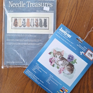 May include: Two cross-stitch kits. One kit features a framed design of various cats with the text "Needle Treasures" and "Des Chats a Volunte". The other kit features a kitten with pansies, with the text "Janlynn" and "Kitten and Pansies".