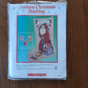 May include: A counted cross stitch pattern for a Christmas stocking featuring a Santa Claus with a bag of gifts and a teddy bear. The stocking is personalised with the name "Kaitlin". The pattern is by Melissa Shirley and is from Dimensions.