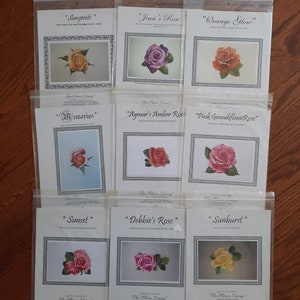 Puede incluir: Nueve patrones de punto de cruz diferentes que presentan varias rosas en diferentes colores, incluidos rojo, rosa, naranja, amarillo y blanco. Cada patrón está titulado con el nombre de la rosa y está enmarcado con un borde blanco. Los patrones están dispuestos en tres filas de tres.
