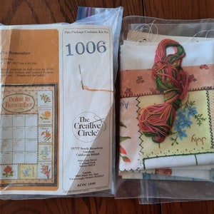 Op de afbeelding: Een kruissteek-borduurset met een witte stof, kleurrijk borduurzijde en instructies voor een kalenderontwerp met de titel "Dates to Remember". De set is verpakt in een doorzichtige plastic zak met een label waarop "The Creative Circle" en "Kit No. 1006" staat.