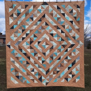 May include: A quilt with a geometric pattern of brown, blue, and white triangles. The quilt is hanging on a clothesline outside.