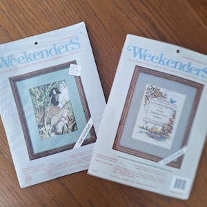 Op de afbeelding: Twee "Weekenders" kruissteekpakketten. Eén toont een gans in een natuurlijke omgeving, de andere een bloemenontwerp met tekst. Beide kits zijn ingelijst en bevatten een passe-partout. De verpakking luidt "leuke privétijdprojecten die in een weekend kunnen worden voltooid."