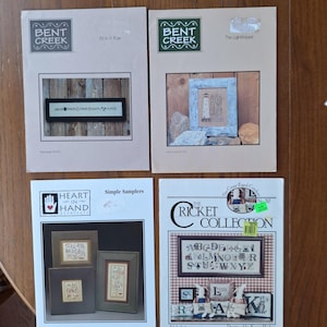 May include: Four cross-stitch pattern booklets. Two feature the "Bent Creek" logo, one titled "All In A Row" and the other "The Lighthouse." The other two booklets are "Heart in Hand" and "The Cricket Collection."
