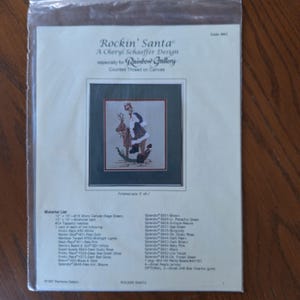 May include: Cross stitch pattern for a Christmas design featuring Santa Claus riding a reindeer. The pattern is titled "Rockin' Santa" and is a Cheryl Schaeffer design for Rainbow Gallery. The finished size is 5 inches by 7 inches.