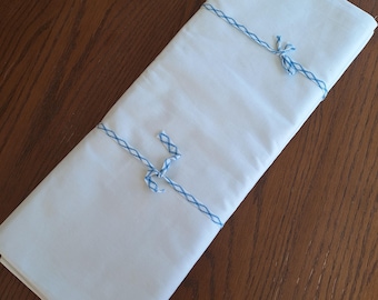 May include: A folded white fabric, secured with blue twine tied in three places. The fabric is rectangular and appears to be a sheet or tablecloth. The twine is a light blue color, and the fabric is a bright white.