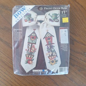May include: A packaged front door bow kit. The bow is 43cm long and features embroidered birdhouse and garden designs with the text "BOW GREETINGS". The kit includes instructions and assorted chart.